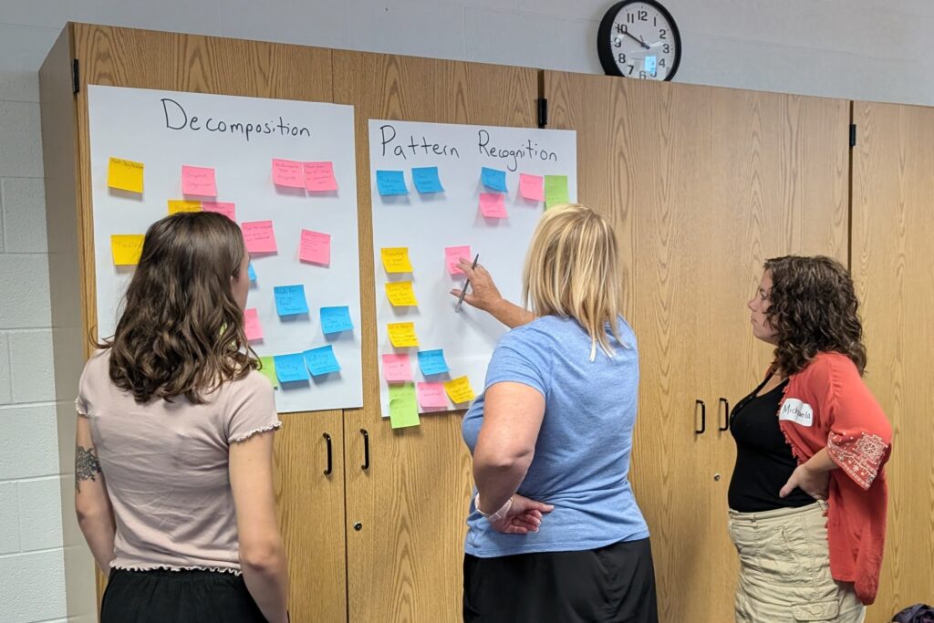 Three teachers standing in front of chart paper discussing  CT ideas with sticky notes